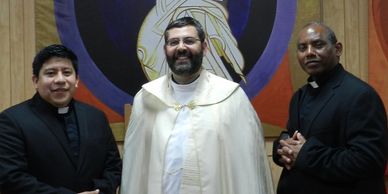 Three clergymen standing indoors wearing religious attire, smiling.