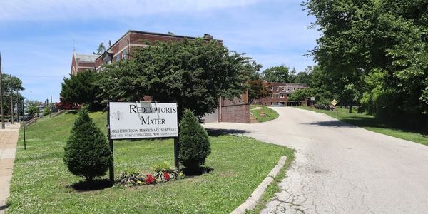 Entrance to Redemptoris Mater with green bushes and a road.