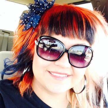 Woman with colorful hair and large sunglasses smiling.