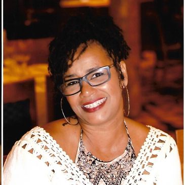 Woman smiling warmly while wearing glasses and earrings.