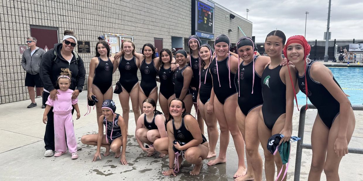 A group of young female water polo players posing together at a poolside.