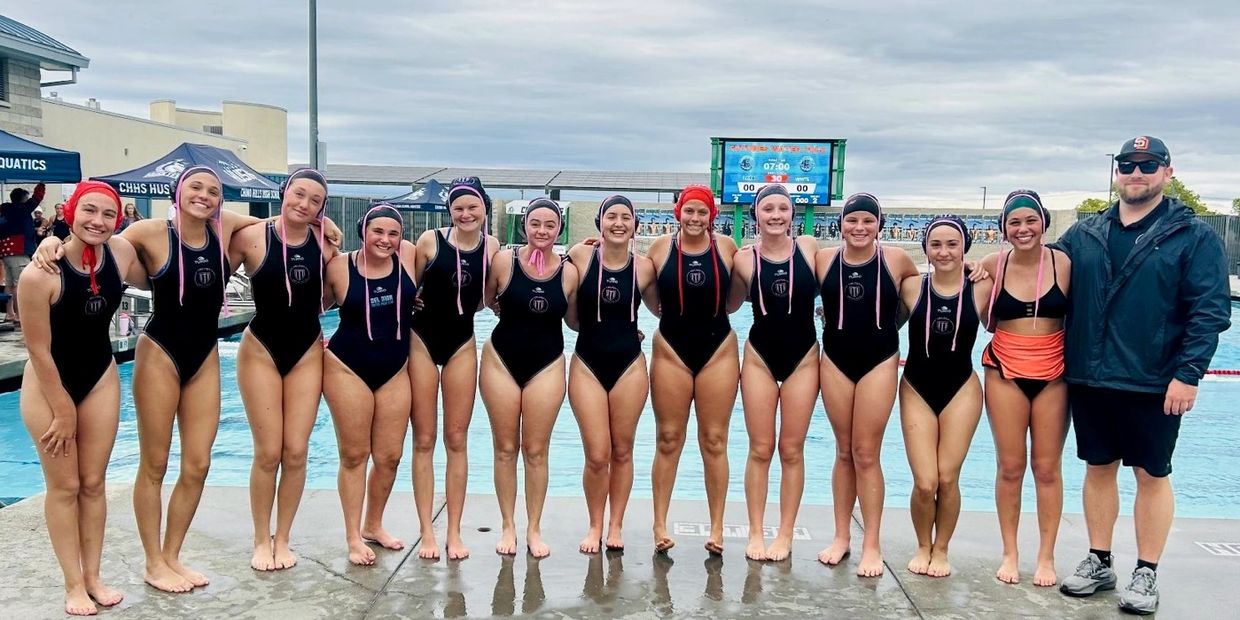 A girls' water polo team with their coach posing by the pool.