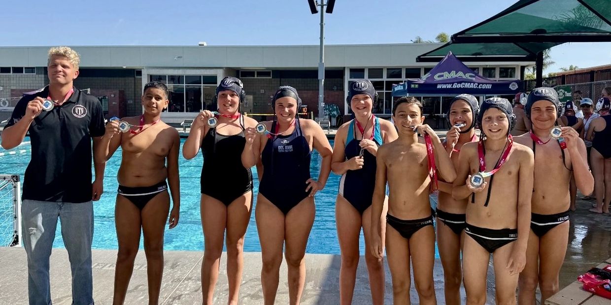 Youth water polo team proudly displaying medals by the pool.