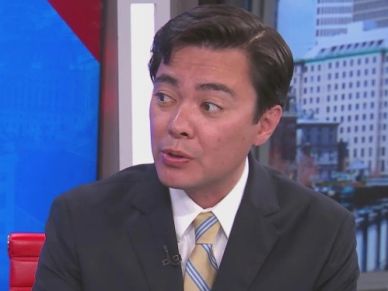 Man in a suit speaking during a TV interview.