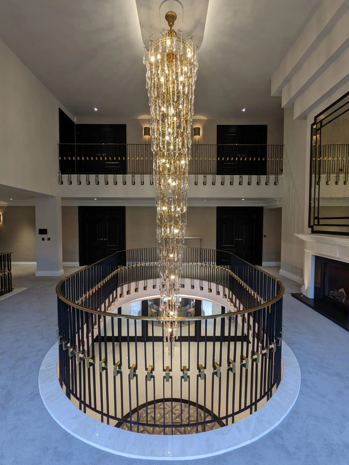 Double-height atrium staircase with a circular ironwork balustrade and cascading chandelier
