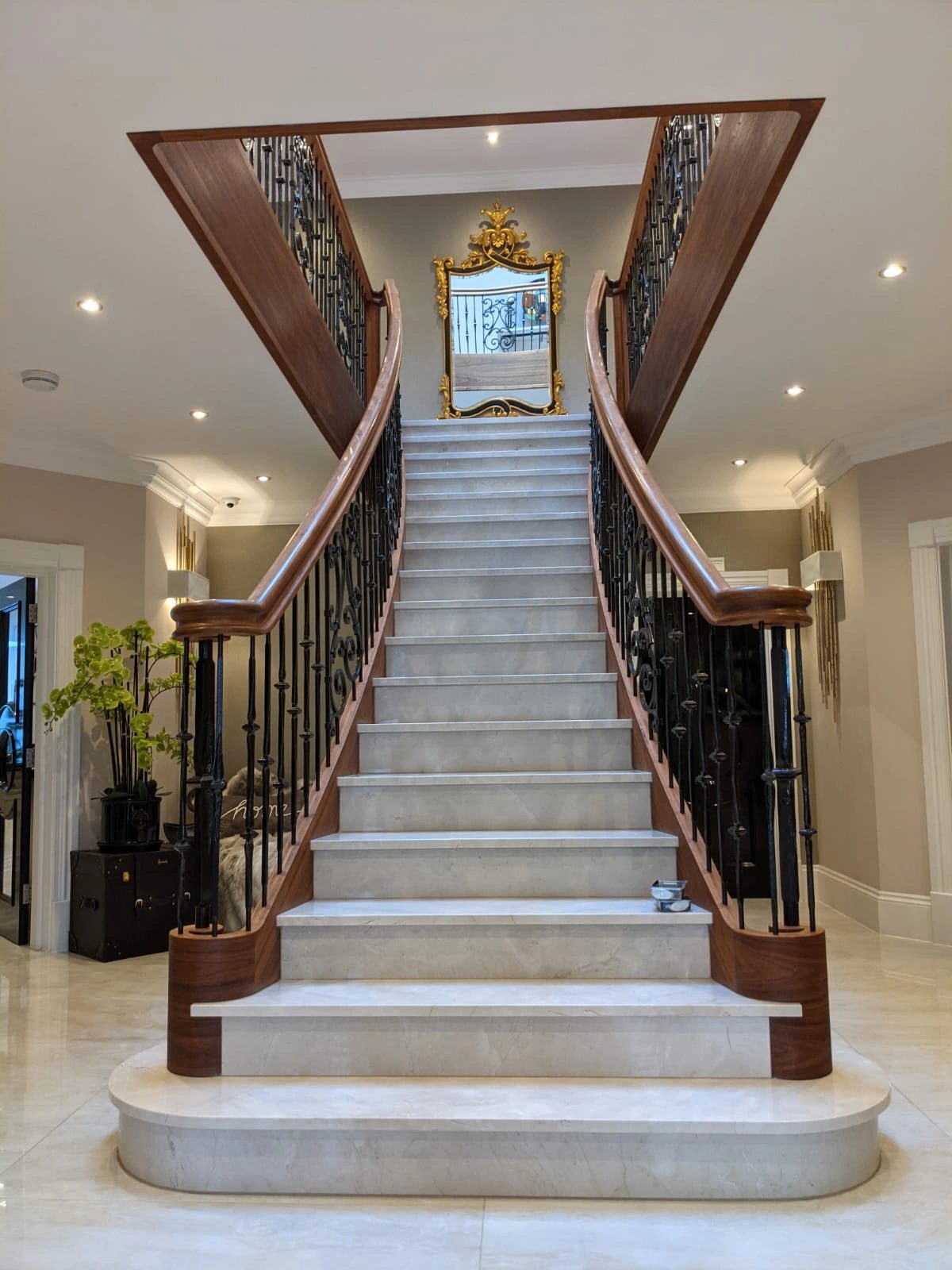 Grand curved stone staircase with hardwood handrail and wrought metal balustrade