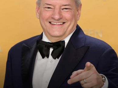 Smiling man in a tuxedo pointing at the camera.