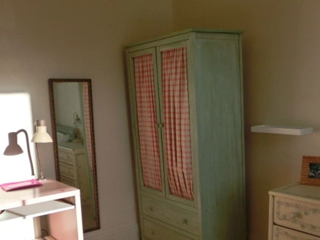 A cozy corner with a wardrobe, mirror, desk, and lamp in soft lighting.