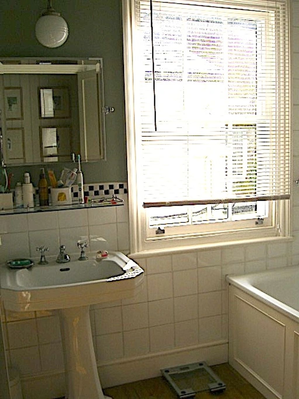 A bathroom with a pedestal sink, bathtub, and window with blinds.
