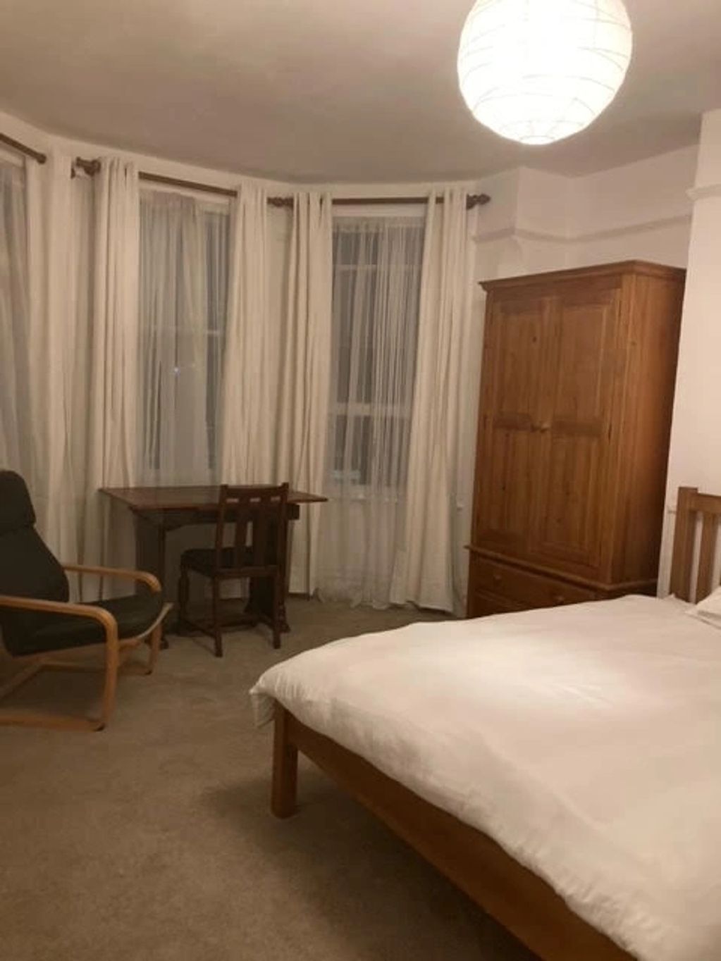 Cozy bedroom with wooden furniture and white curtains.