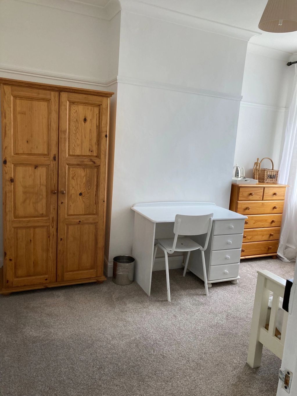 Simple bedroom corner with wooden furniture and a white desk.
