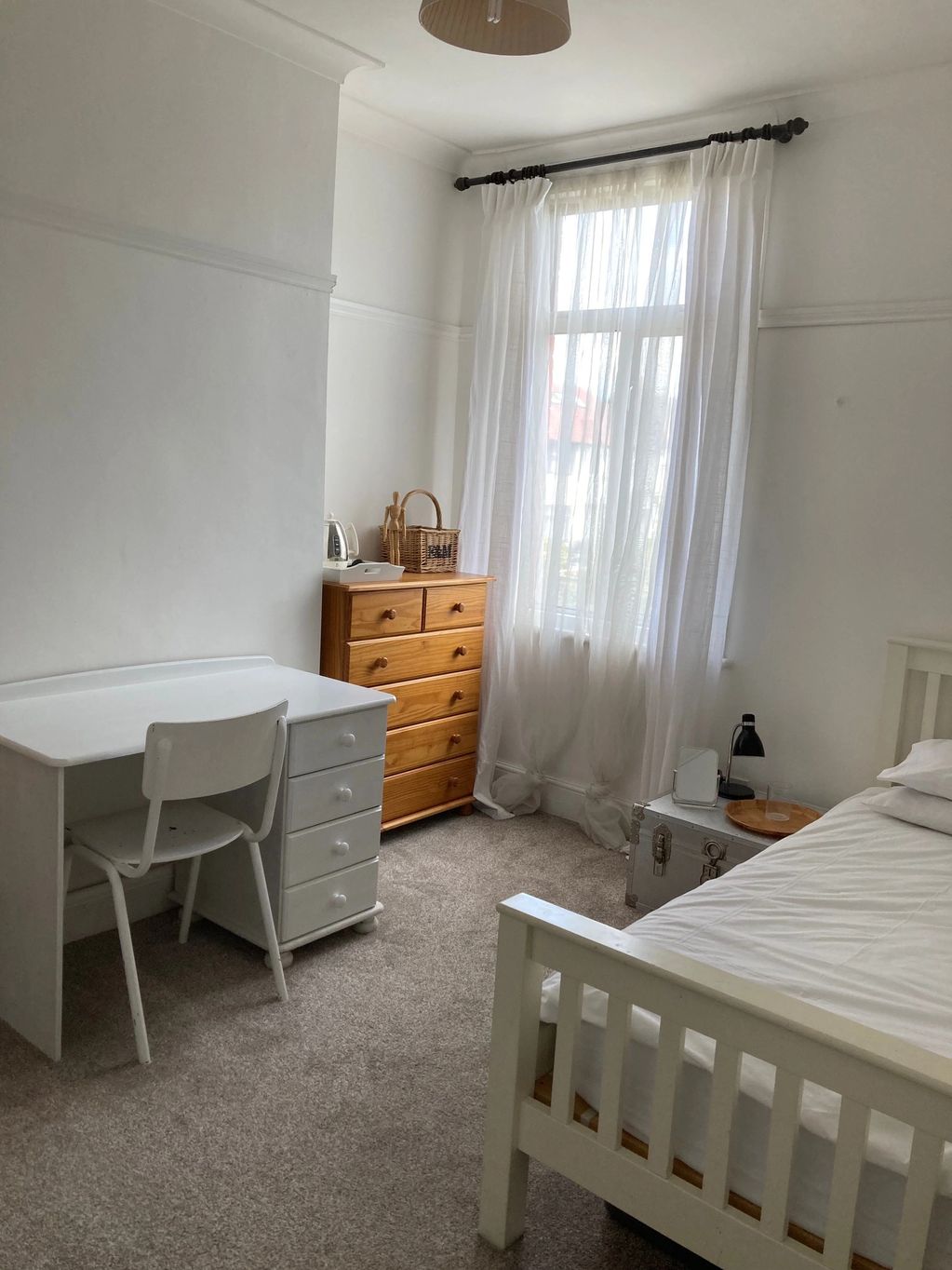 Cozy bedroom with white furniture and natural light from a large window.
