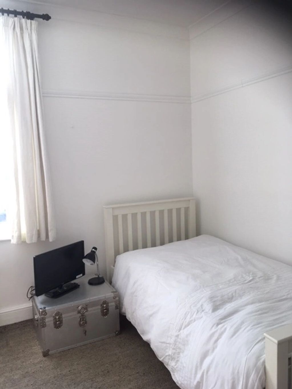 A minimalistic bedroom with a white bed and metal trunk as a nightstand.