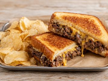 Grilled cheese sandwich with beef and potato chips.