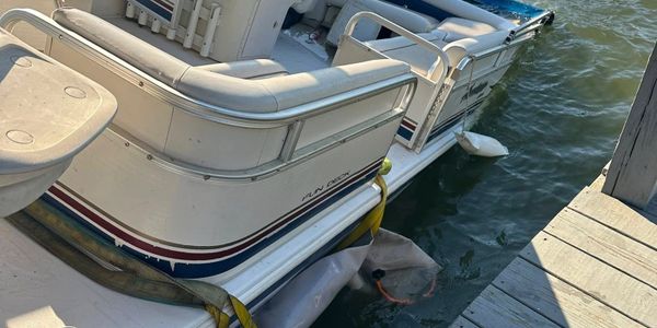 Pontoon boat docked by a wooden pier on calm water.