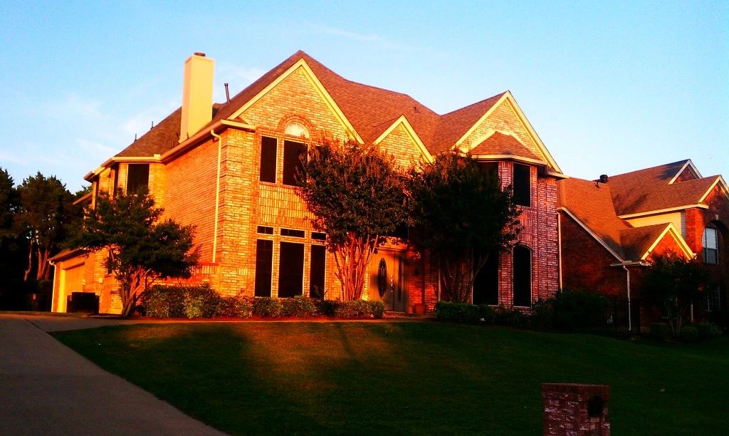Large brick house illuminated by warm sunlight with a green lawn.