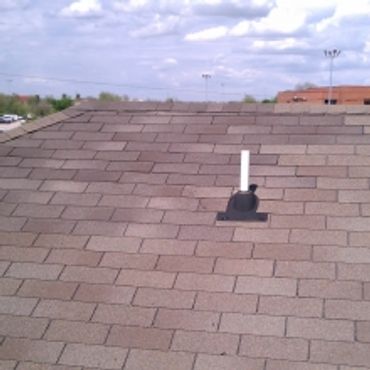 Shingled roof with a vent pipe under a blue sky with clouds.