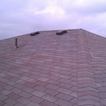 Asphalt shingle roof with vents under a cloudy sky.