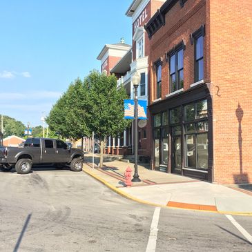 Street view of a small-town downtown with brick buildings and parked vehicles.