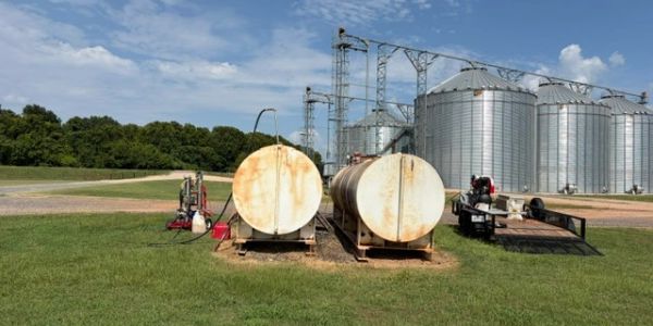Rusty fuel tanks near grain silos in a rural setting.