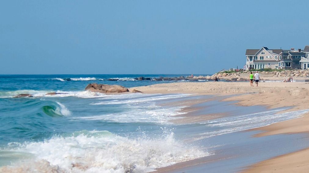 A serene beach with waves crashing and houses in the background.