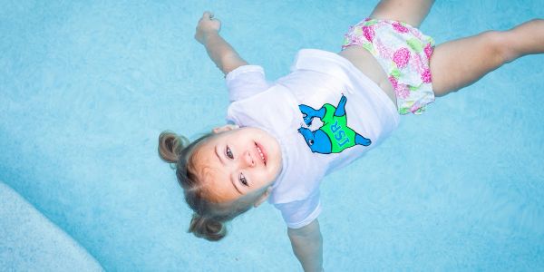 Child floating in a pool, smiling.