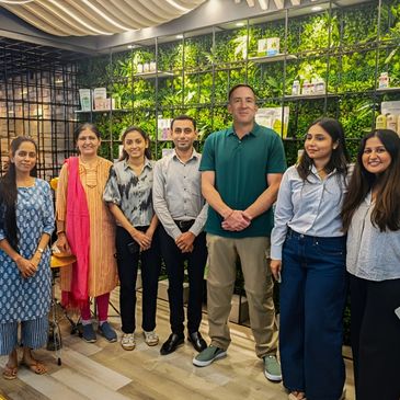 Group photo of seven people standing indoors with a green plant wall backdrop.