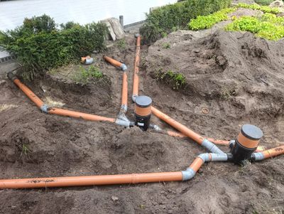 Underground orange drainage pipes being installed in a garden area.