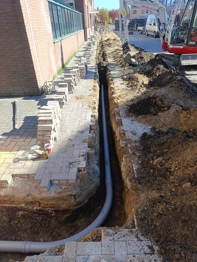 Construction site with a trench and buried pipe along a sidewalk.