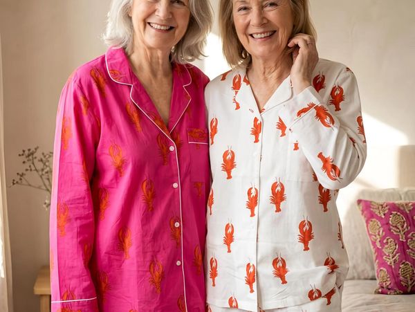 Two smiling elderly women in lobster print pyjamas standing indoors.