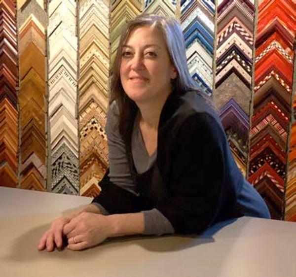 Woman leaning on a table with colorful picture frame samples behind her.