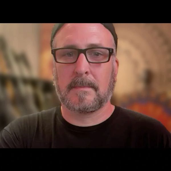 Man with glasses and beard wearing a black shirt and cap.