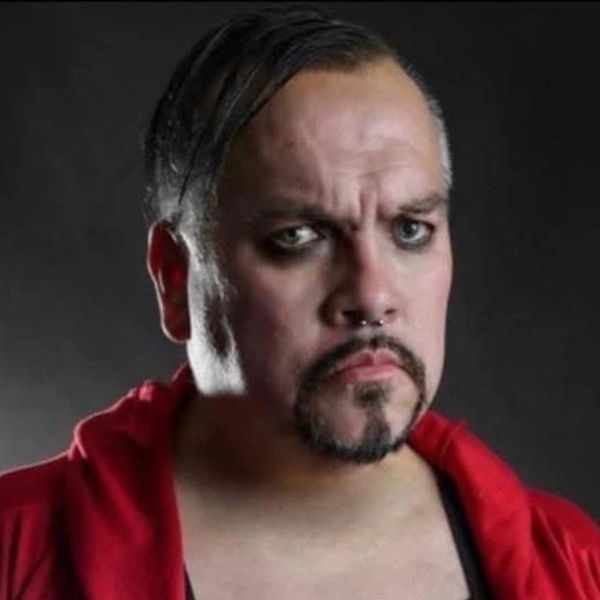 Man with dark eyeliner and a serious expression in a red jacket.