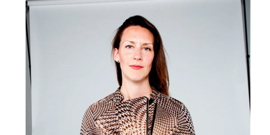 A woman stands confidently against a plain backdrop.