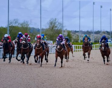 Jockeys racing horses on a dirt track during a horse race.