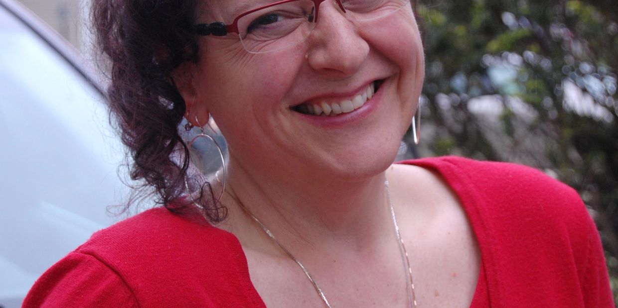 Smiling woman in red sweater with glasses and hoop earrings.