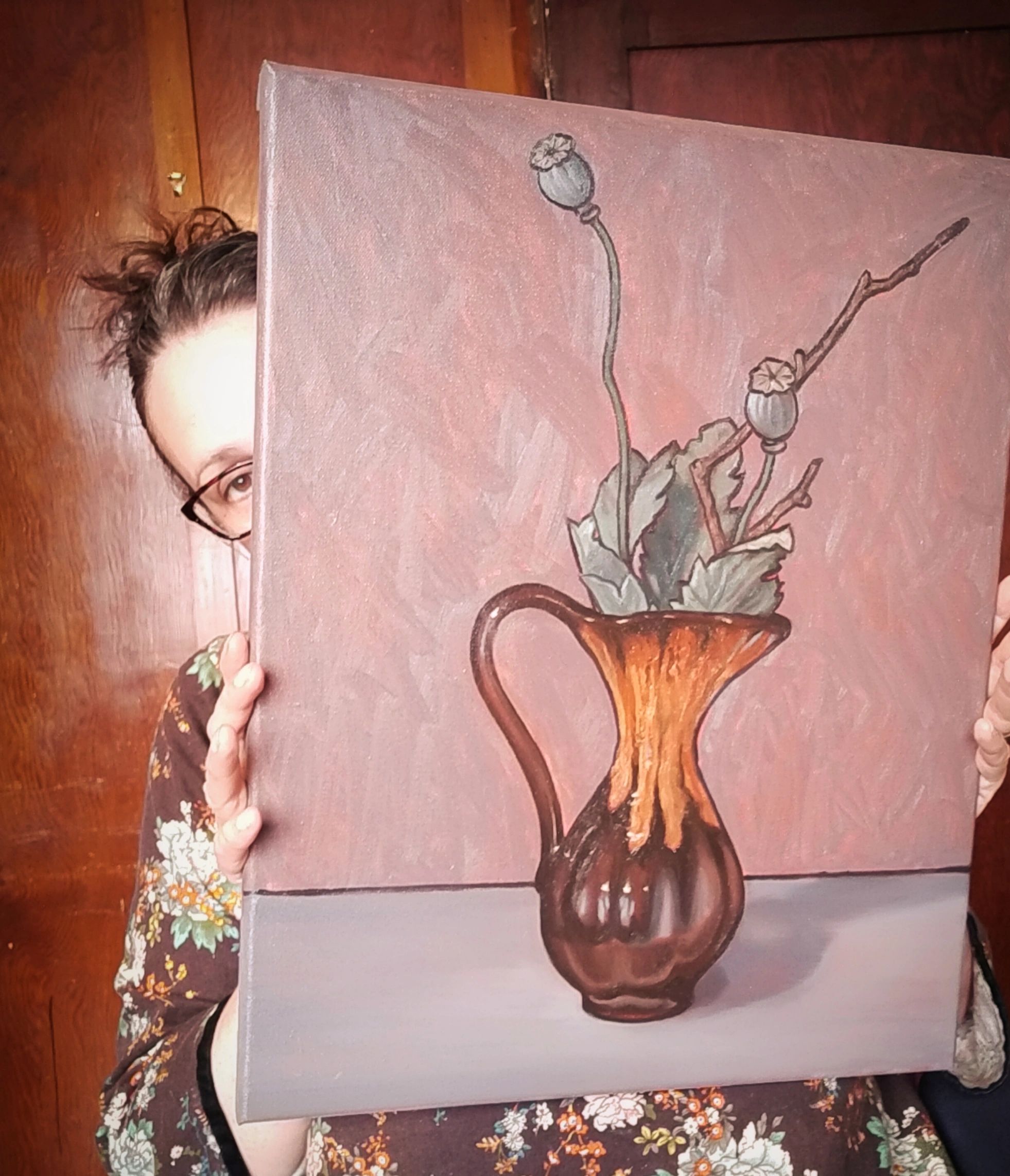 Artist Jonette Murray peeks out from behind a painting of a retro jug and poppy seeds