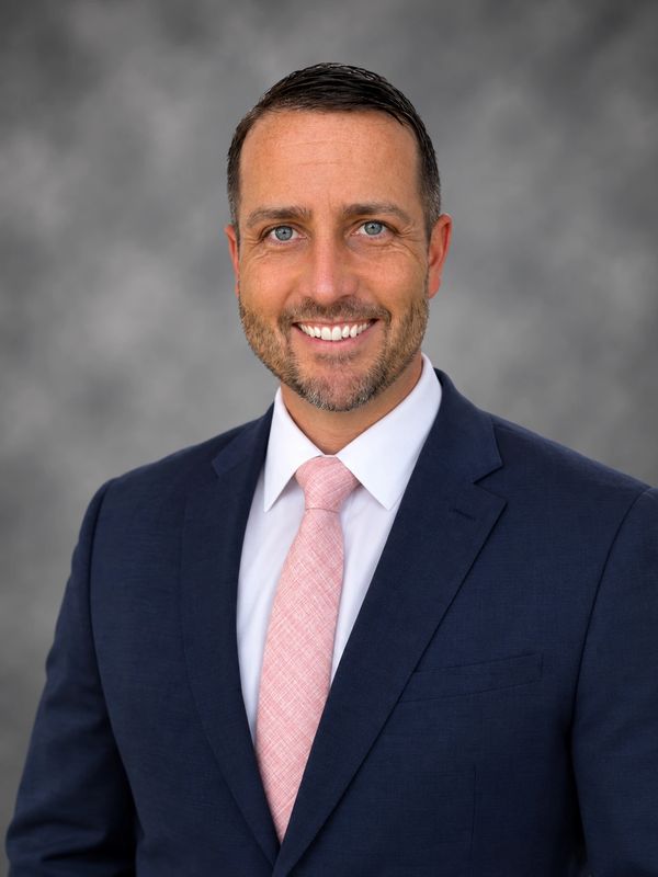 Man in navy suit with a pink tie smiling.