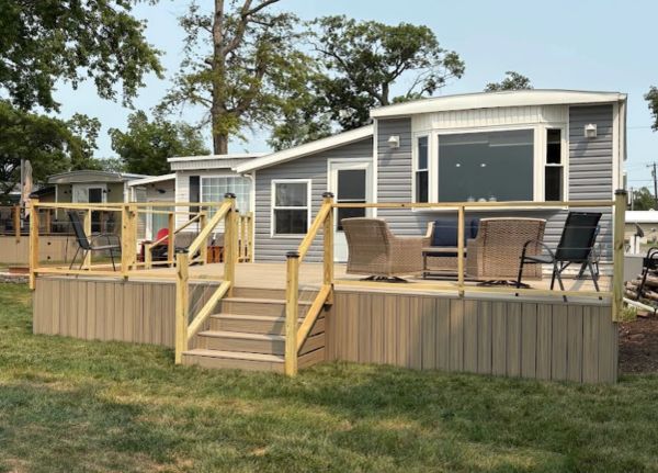 Modern mobile home with wooden deck and outdoor furniture.
