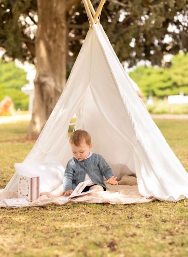 Baby reading inside a white tent outdoors.