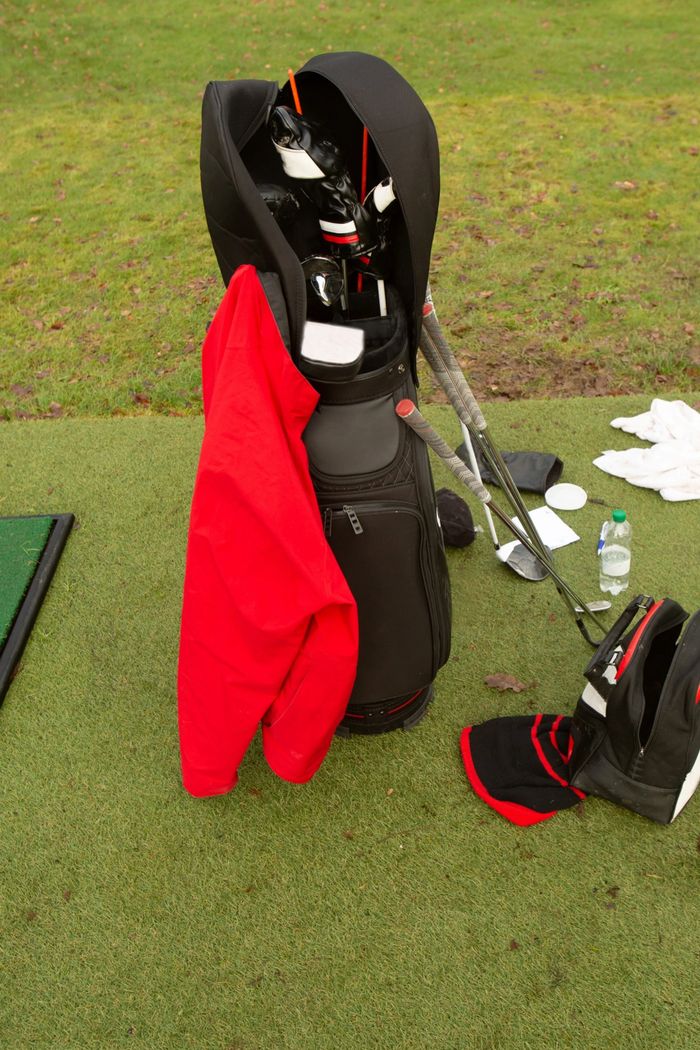 Golf bag with clubs and a red jacket on a grassy field.