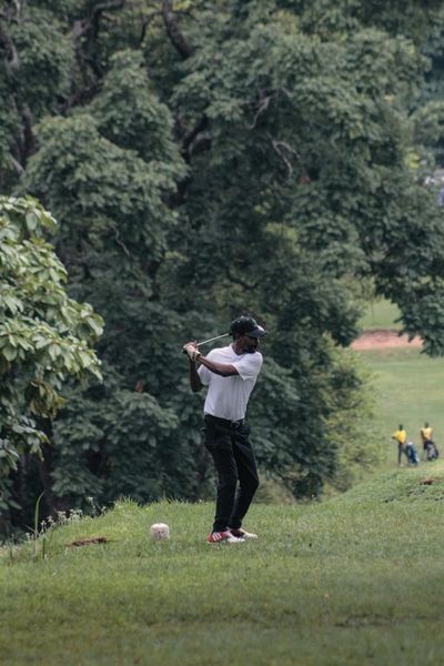 Man playing golf on a grassy course surrounded by trees.