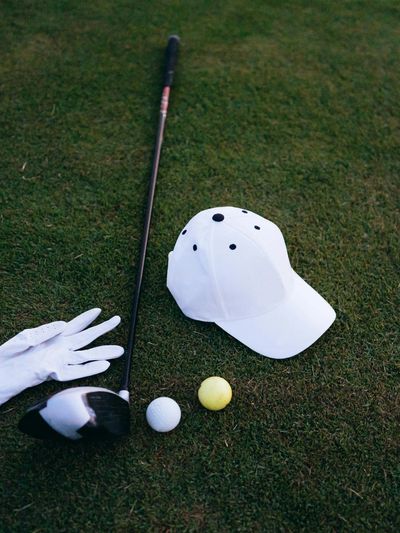 Golf gear on grass including a club, balls, glove, and cap.
