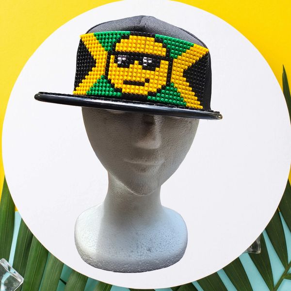 A bold black snapback hat featuring a pixel art patch in green, yellow, and black LEGO-style bricks.