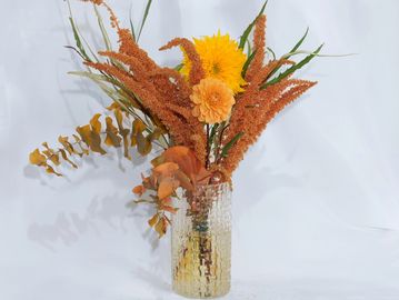 autumn colors bouquet in a clear glass vase in front of a white background