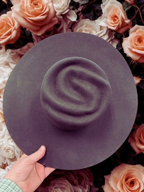 Hand holding a unique black hat with a swirl design against a backdrop of roses.