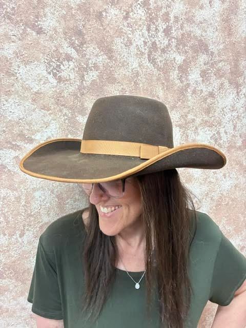 Woman smiling wearing a large brown cowboy hat and glasses.