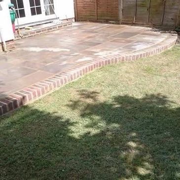 Clean backyard patio with brick edging and green lawn.