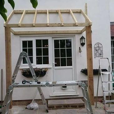 Wooden frame construction outside a door with ladders and tools.