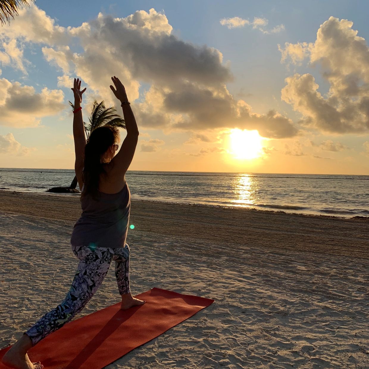 Person doing yoga on beach at sunset.